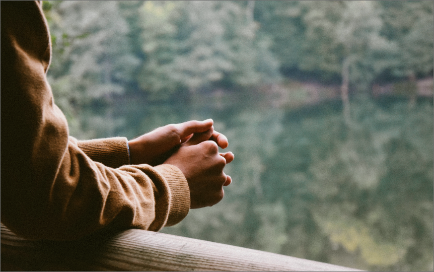 two hands reflected in a window looking out over green